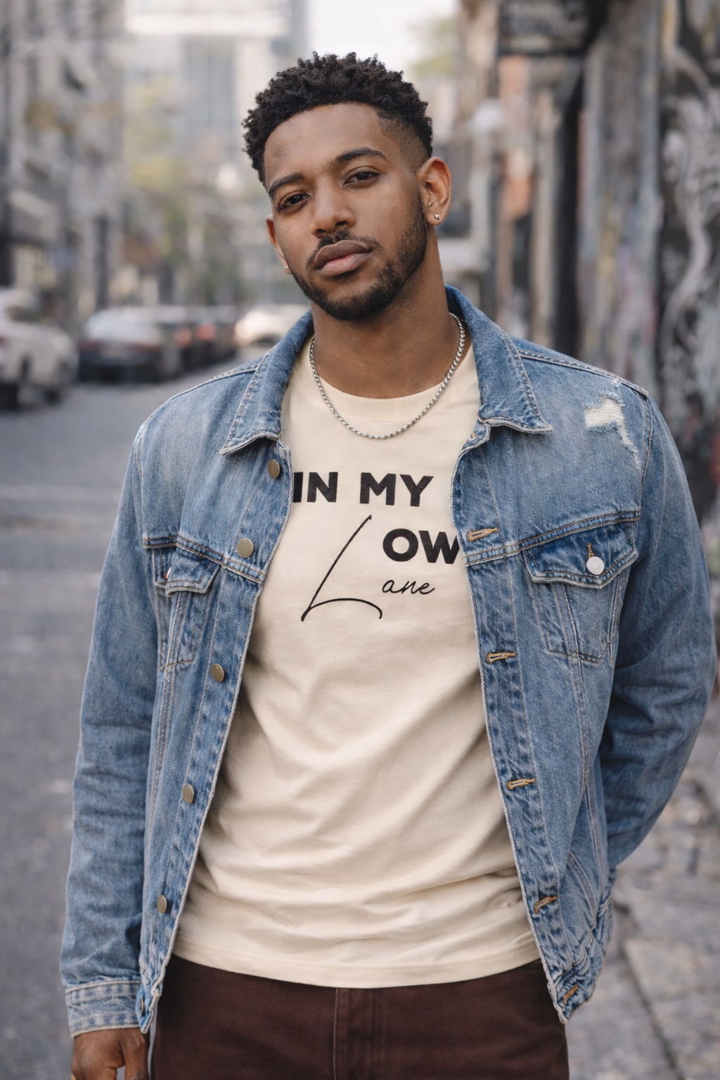 Man wearing denim jacket over a cream streetwear t-shirt styled as casual urban outfit